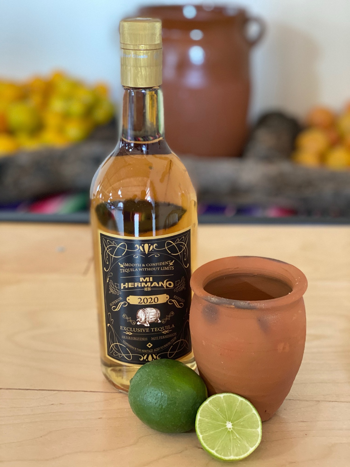 Mi Hermano bottle beside a clay cup and fresh limes