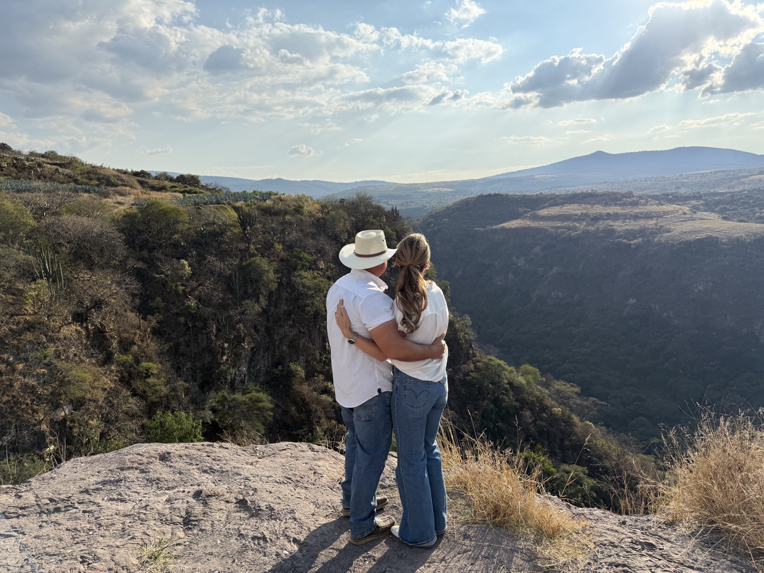 Two people embracing as they look across a sunlit canyon
